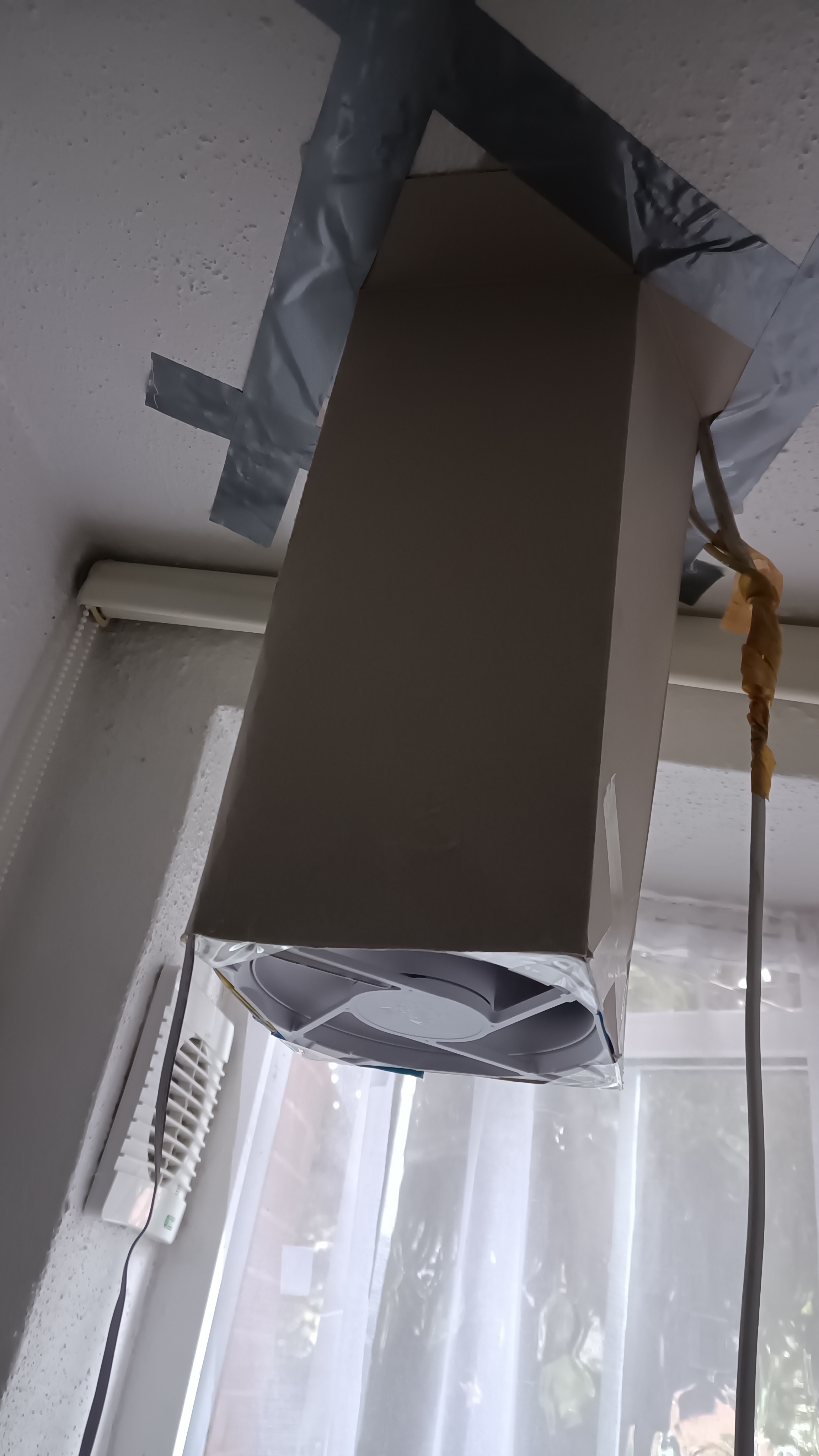 A computer case fan connected to a hole in the ceiling with a "duct" made of cardboard from a cereal box.